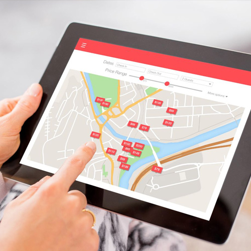 A hand using a tablet showing a hotel booking map with room rates marked across a city