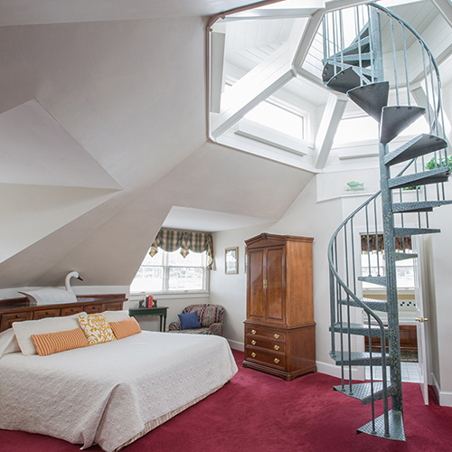 A guest room with a spiral staircase leading to a skylit loft above the bed