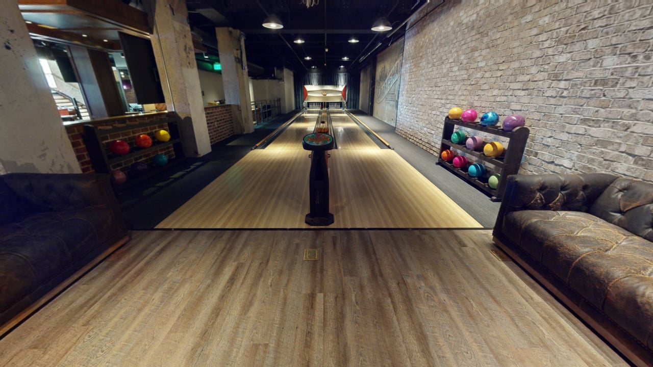 A two-lane bowling alley inside a bar, with exposed brick walls and worn leather sofas