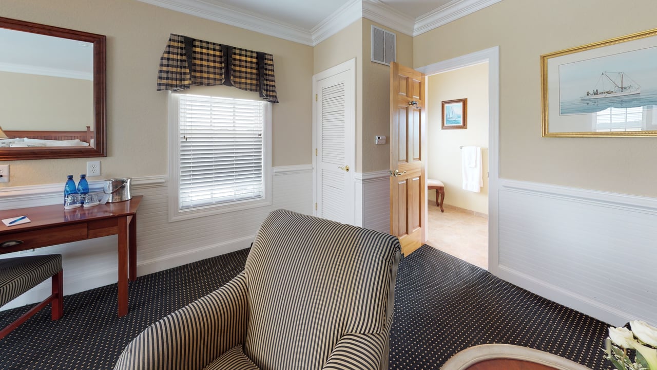 A guest suite with a seating area, writing desk, and an adjoining room beyond an open door