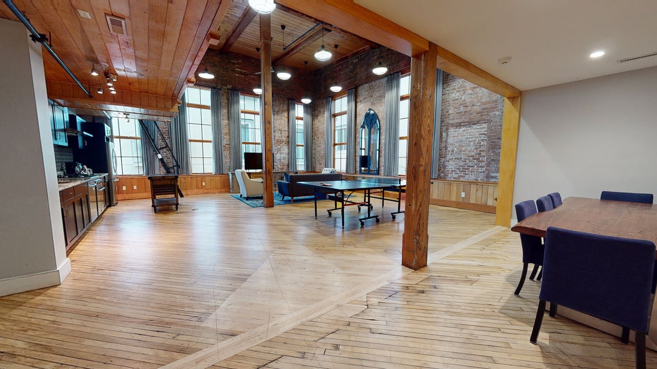 A timber-beamed loft suite with exposed brick, tall windows, a table tennis table and a long dining table