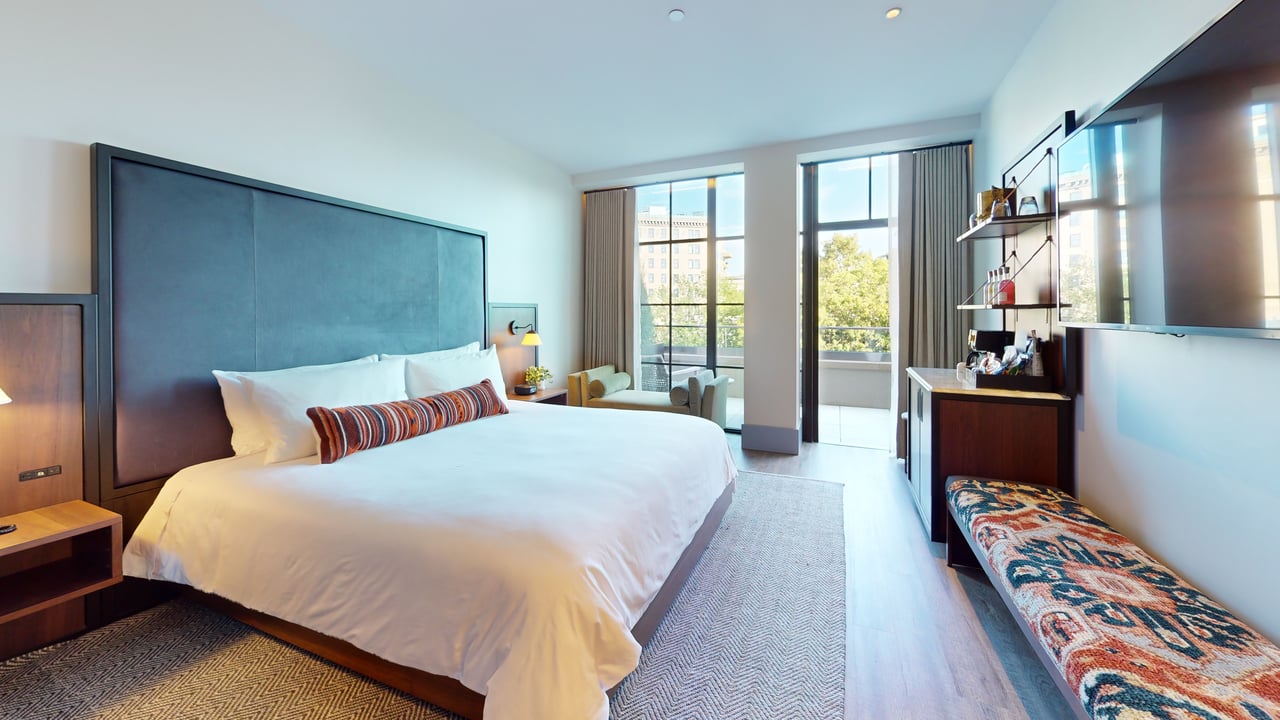 A king guest room with a teal upholstered headboard, opening through glass doors onto a private terrace
