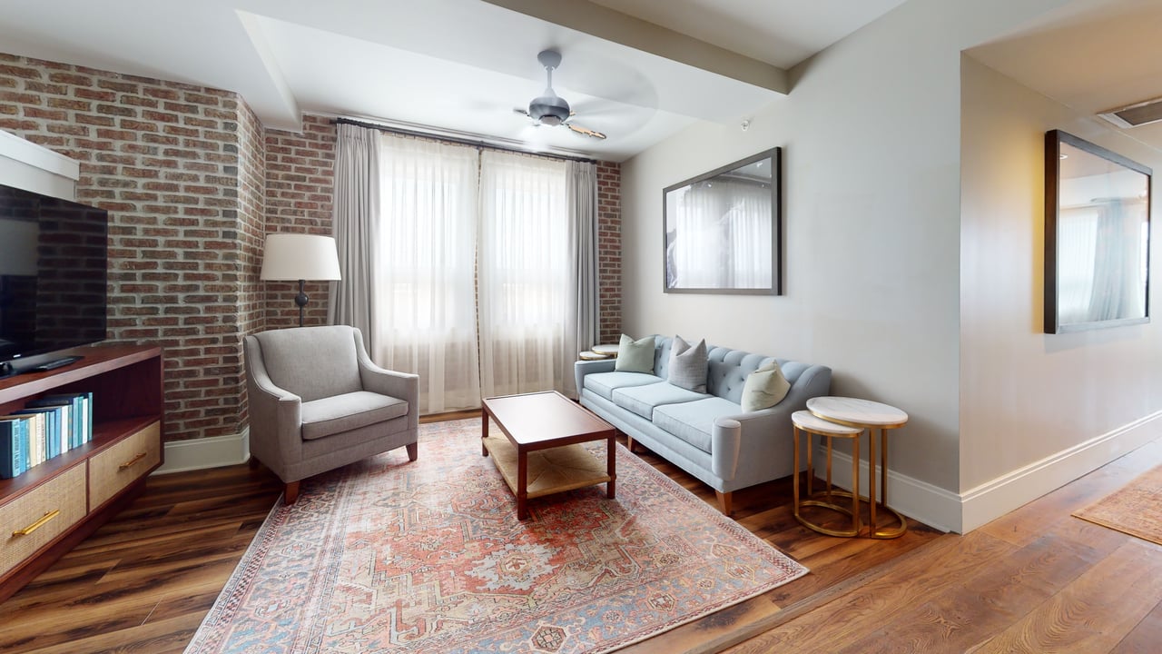 A suite living area with exposed brick walls, a pale blue sofa and a patterned rug on wood floors