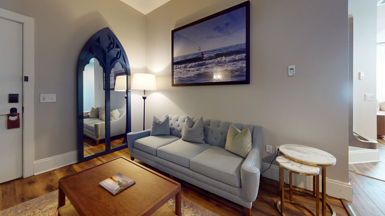 A suite sitting room with a grey sofa, arched floor mirror and hardwood floors