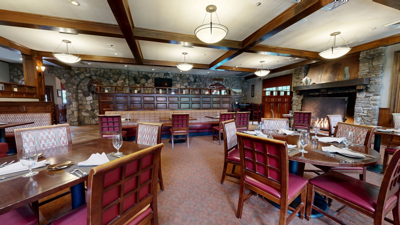 A restaurant dining room with a stone fireplace, coffered wood ceiling and red upholstered chairs